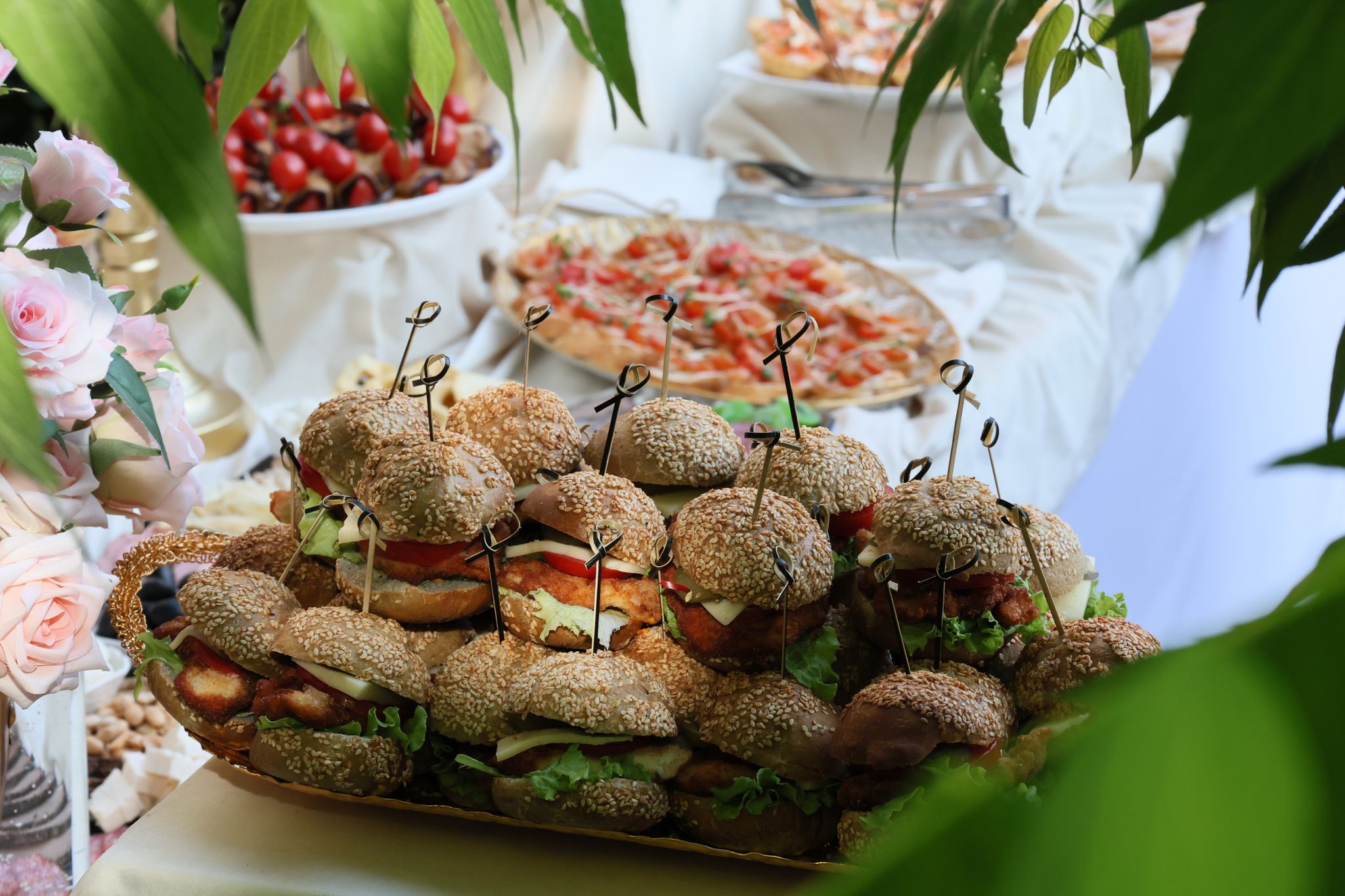 A delightful spread of sandwiches and pizzas at an elegant party setting, surrounded by flowers and greenery.